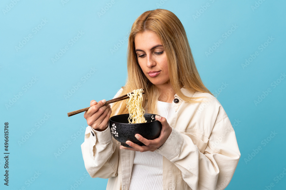 Young Uruguayan blonde woman over isolated blue background holding a bowl of noodles with chopsticks Young Uruguayan blonde woman over isolated blue background holding a bowl of noodles with chopsticks