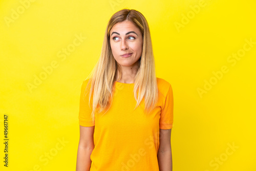Blonde Uruguayan girl isolated on yellow background making doubts gesture looking side
