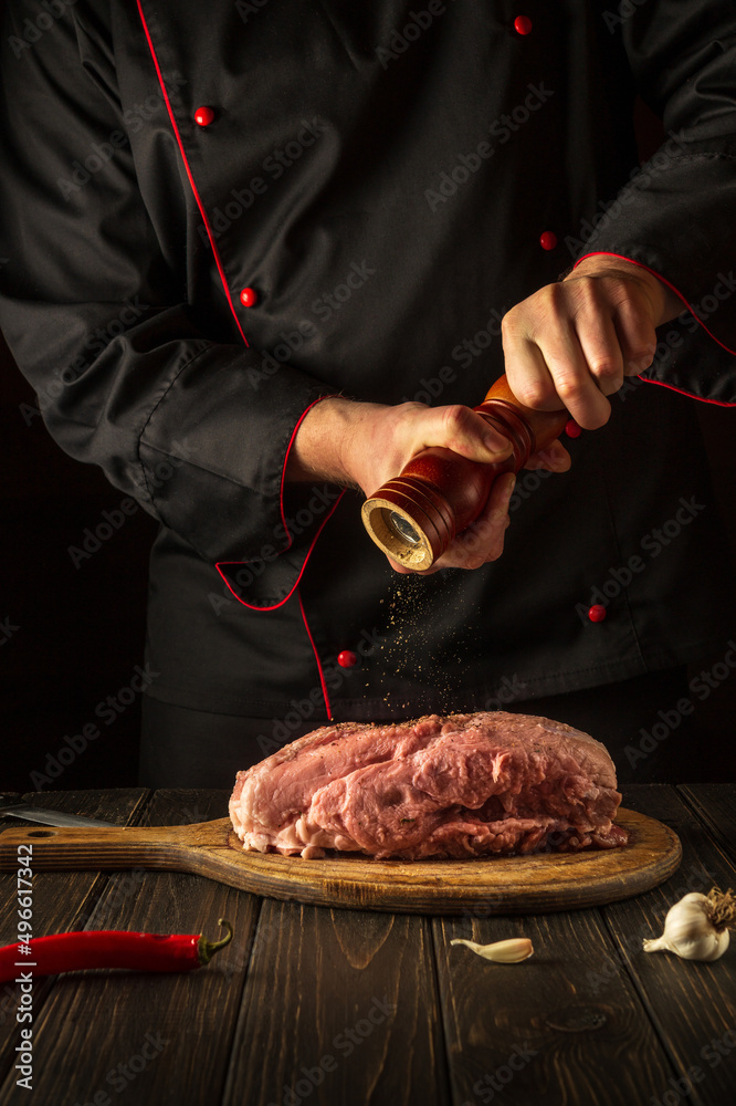 Chef prepares raw veal meat. Before baking, the chef adds pepper to the beef. National dish is being prepared in the kitchen