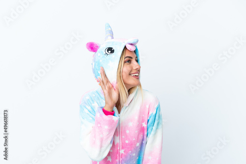 Blonde Uruguayan girl wearing a unicorn pajama isolated on white background listening to something by putting hand on the ear