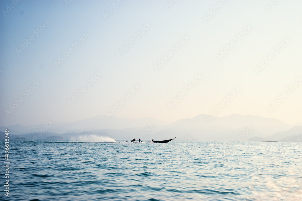 Beautiful идгу seascape with traditional thai longtail boat and rocks on horizon.