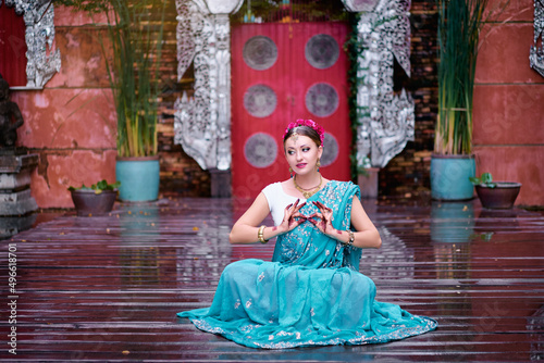 Beautiful young caucasian woman in traditional indian clothing with bridal makeup and jewelry. Bollywood dancer in Sari and henna on hands meditating at temple garden.