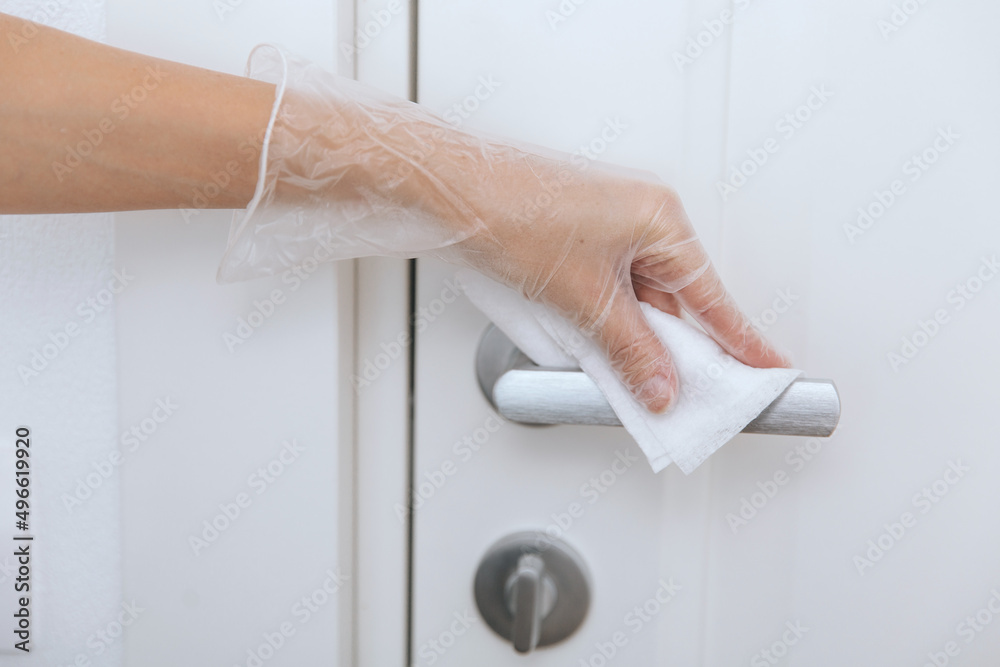 Cleaning door handles with wet wipe and white gloves. Sanitize surfaces prevention in hospital and public spaces against corona virus. Woman hand using towel for cleaning home room door link.