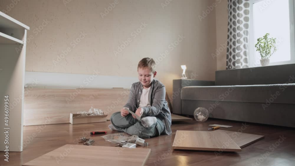 Caucasian boy sits on floor among details of chipboard furniture and various fixtures. Child shows gray furniture handle to domestic hamster. White pet runs around the room in large transparent ball. Caucasian boy sits on floor among details of chipboard furniture and various fixtures. Child shows gray furniture handle to domestic hamster. White pet runs around the room in large transparent ball.