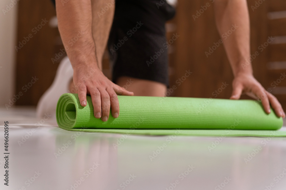 Unwinding roll mat, preparing a place for sports fitness man. Determined guy doing physical training. Strong handsome young man, an a gym