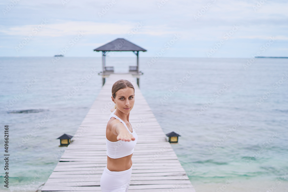 Happy young woman standing in yoga pose on wooden pier. Practicing yoga with ocean beach in the background. Happy young woman standing in yoga pose on wooden pier. Practicing yoga with ocean beach in the background.