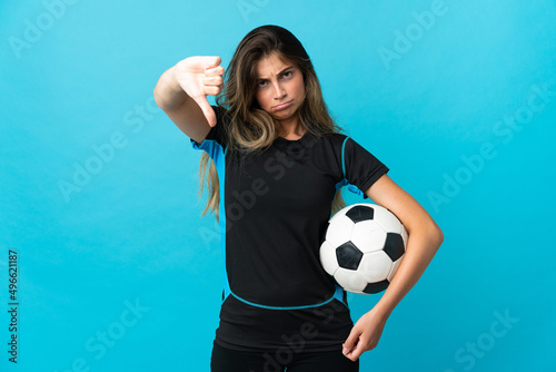 Young football player woman isolated on blue background showing thumb down with negative expression