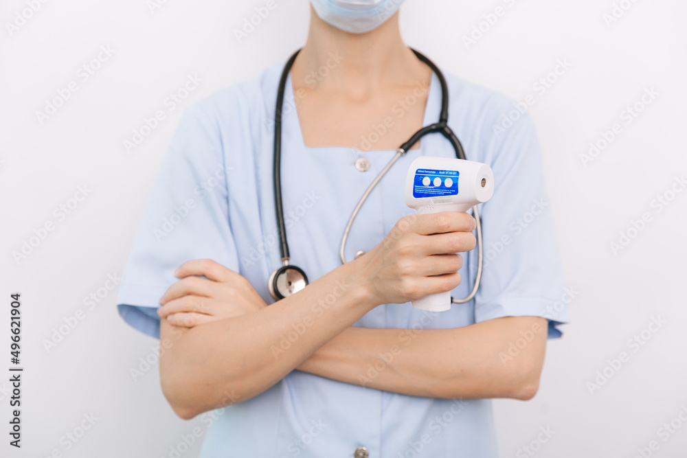 Temperature measurement gun in doctor hands. Close-up shot of doctor wearing protective surgical mask ready to use infrared isometric thermometer gun to check body temperature for virus symptoms. Temperature measurement gun in doctor hands. Close-up shot of doctor wearing protective surgical mask ready to use infrared isometric thermometer gun to check body temperature for virus symptoms.