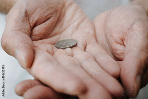 Coin in wrinkled hands, senior caucasian man holding money in his palms close-up. Concept of poverty, bankruptcy, pension, financial problems. Macro photo, selective focus
