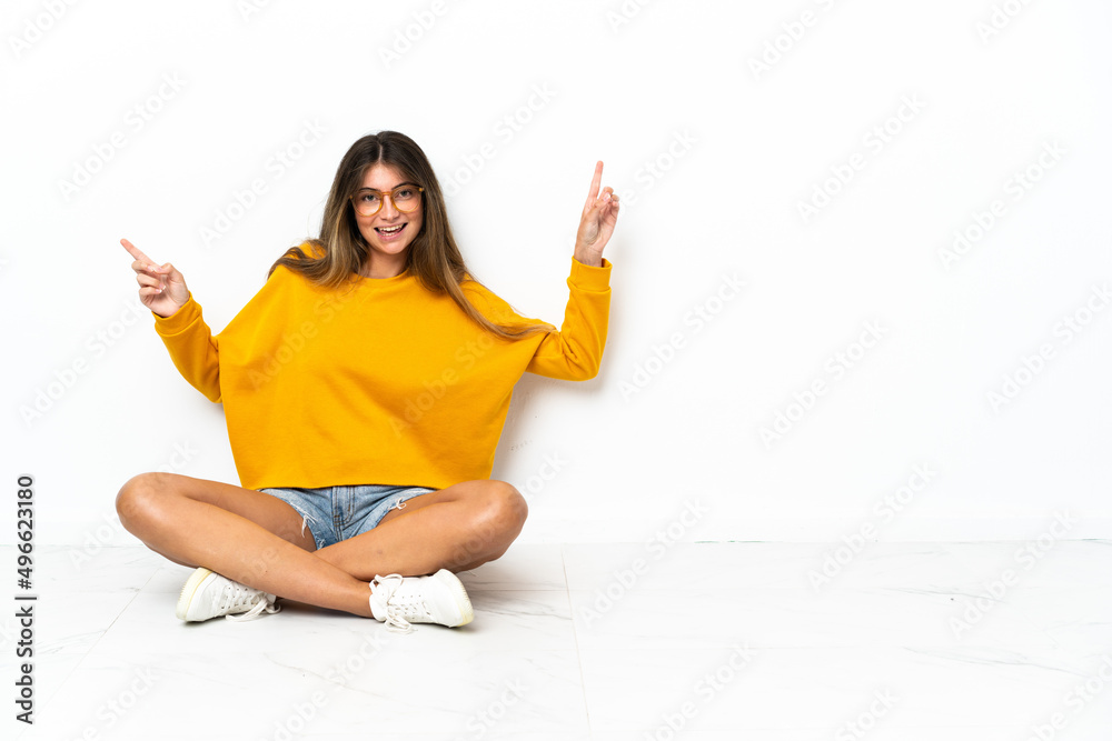 Young woman sitting on the floor isolated on white background pointing finger to the laterals and happy Young woman sitting on the floor isolated on white background pointing finger to the laterals and happy