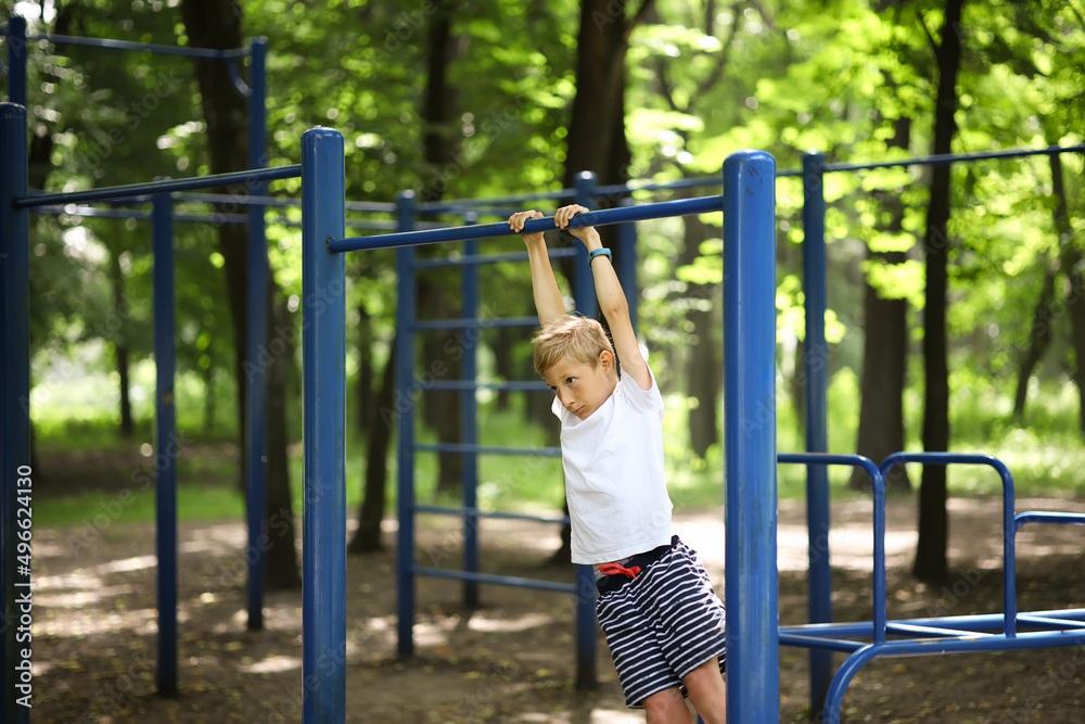 the boy goes in for sports in the park hung on the horizontal bar and sways