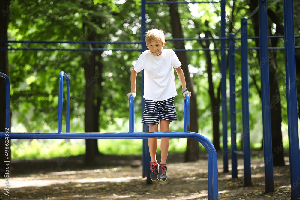 athlete boy in the park hung on his hands and does exercises on the uneven bars athlete boy in the park hung on his hands and does exercises on the uneven bars