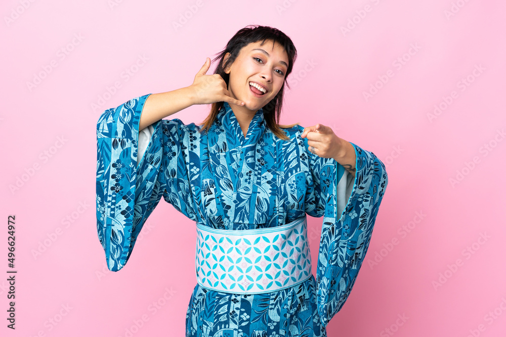 Young woman wearing kimono over isolated blue background making phone gesture and pointing front Young woman wearing kimono over isolated blue background making phone gesture and pointing front
