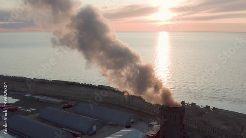 Evening sunset and blue sea Drone removes the chimney releases black smoke. The coal processing factory pollutes the environment with the release of toxic gases.
