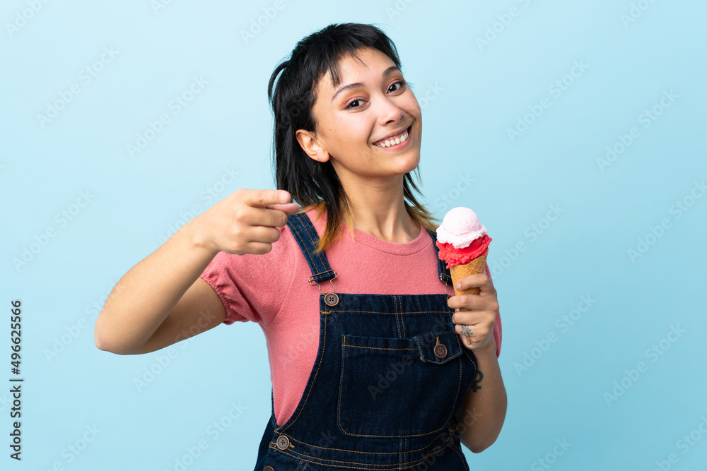 Young Uruguayan girl holding a cornet ice cream over isolated blue background points finger at you with a confident expression Young Uruguayan girl holding a cornet ice cream over isolated blue background points finger at you with a confident expression