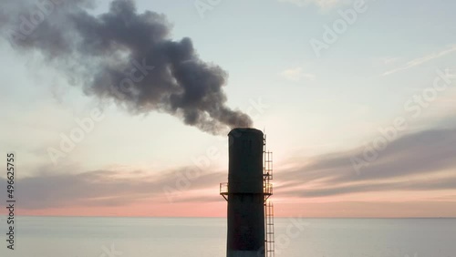 Evening sunset and blue sea Drone removes the chimney releases black smoke. The coal processing factory pollutes the environment with the release of toxic gases.