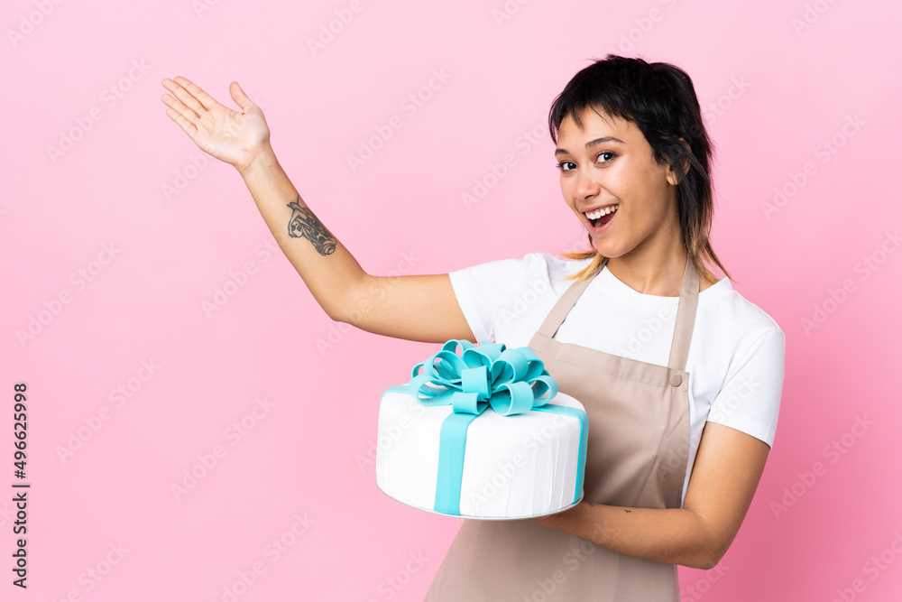 Uruguayan Pastry chef holding a big cake over isolated pink background extending hands to the side for inviting to come