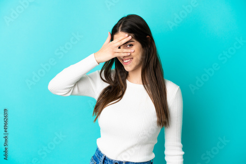 Young caucasian woman isolated on blue background covering eyes by hands and smiling