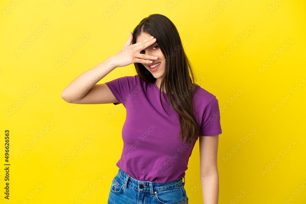 Young caucasian woman isolated on yellow background covering eyes by hands and smiling Young caucasian woman isolated on yellow background covering eyes by hands and smiling