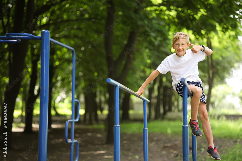Fototapeta premium sports boy climbed on the bar for push-ups and laughs showing thumbs up