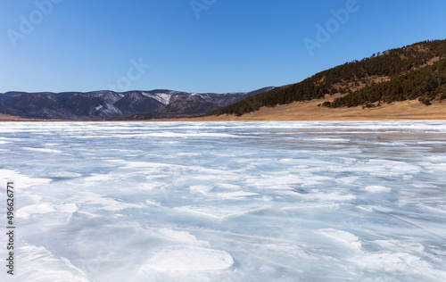 Baikal Lake in early spring on sunny day. Ice surface was covered with thawed patches and snow on ice became loose and wet. Coastal hill cleared of snow. Beautiful spring landscape. Natural background