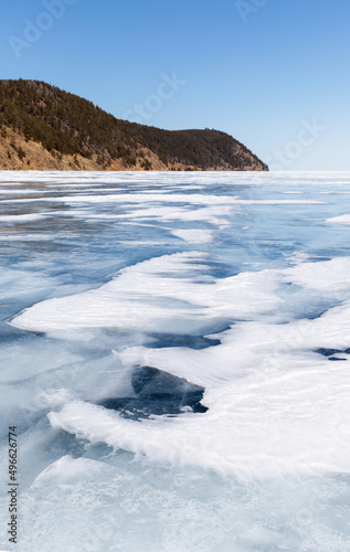 Early spring at Baikal Lake. Beautiful landscape with blue ice surface with thawed patches at sunny day. Natural lakeside background. Spring ice travel and outdoors