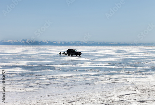 Baikal Lake on a sunny day in early spring. People relax on the ice of the lake, have a picnic and admire the mountain scenery on a Sunday afternoon. Family vacation in nature concept