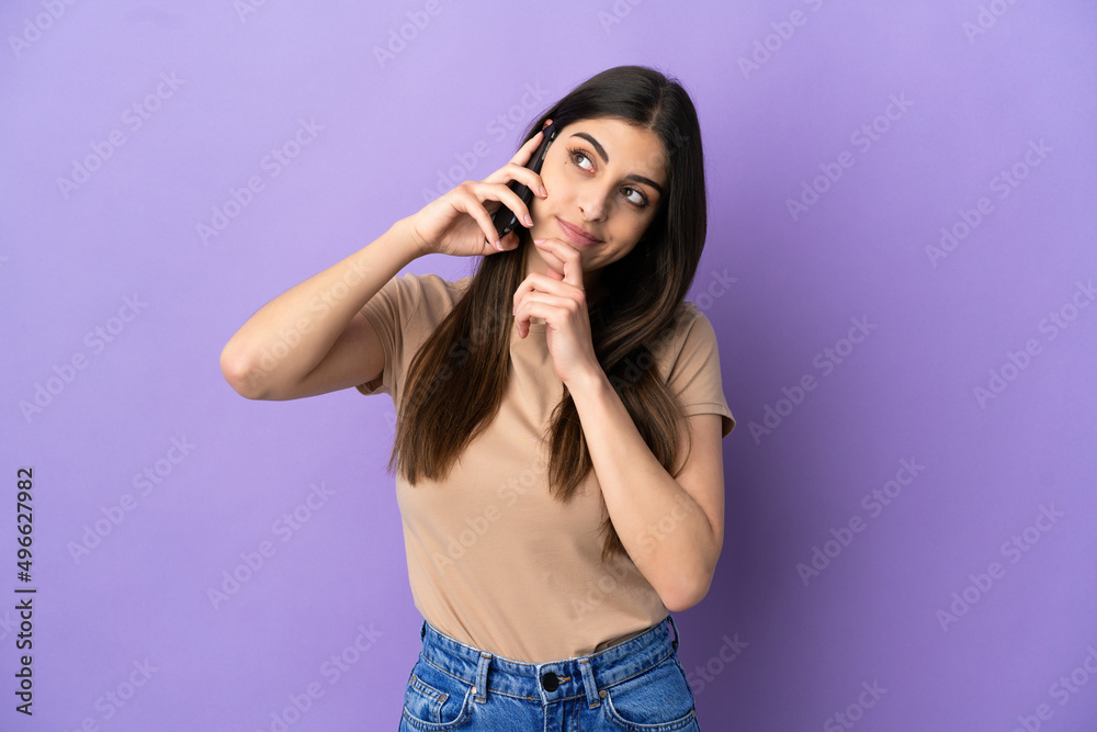 Young caucasian woman using mobile phone isolated on purple background and looking up Young caucasian woman using mobile phone isolated on purple background and looking up