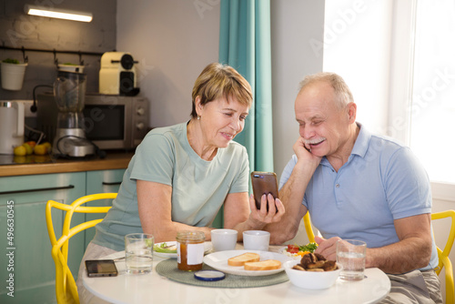 Senior couple eating breakfast and using smartphone at home. elderly couple watches news or video on a smartphone