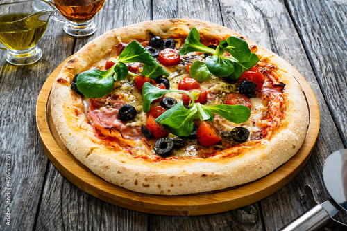 Circle prosciutto pizza with mozzarella, pork ham and black olives on wooden table

