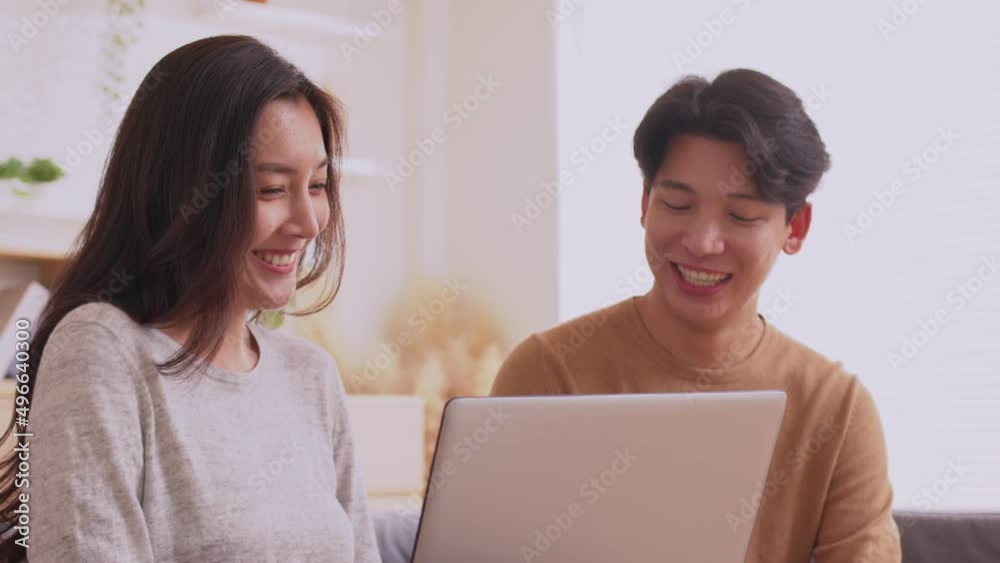 At home in the living roomm.Asian couple working and researching online on labtop while sitting on sofa. At home in the living roomm.Asian couple working and researching online on labtop while sitting on sofa.