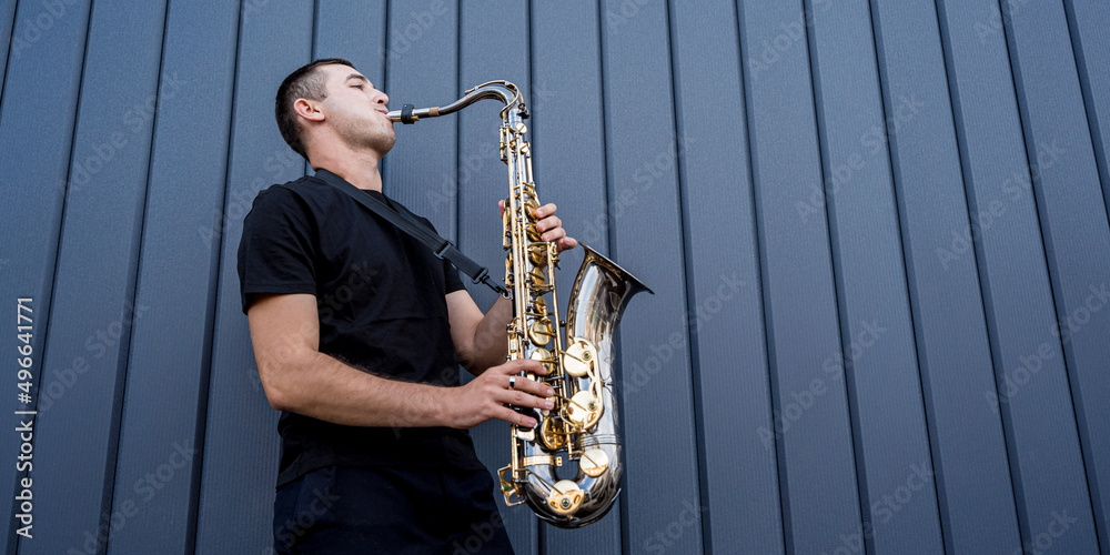 Obraz premium Young street musician playing saxophone near the big blue wall