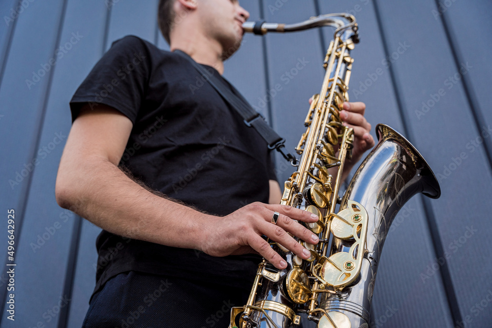Obraz premium Young street musician playing saxophone near the big blue wall