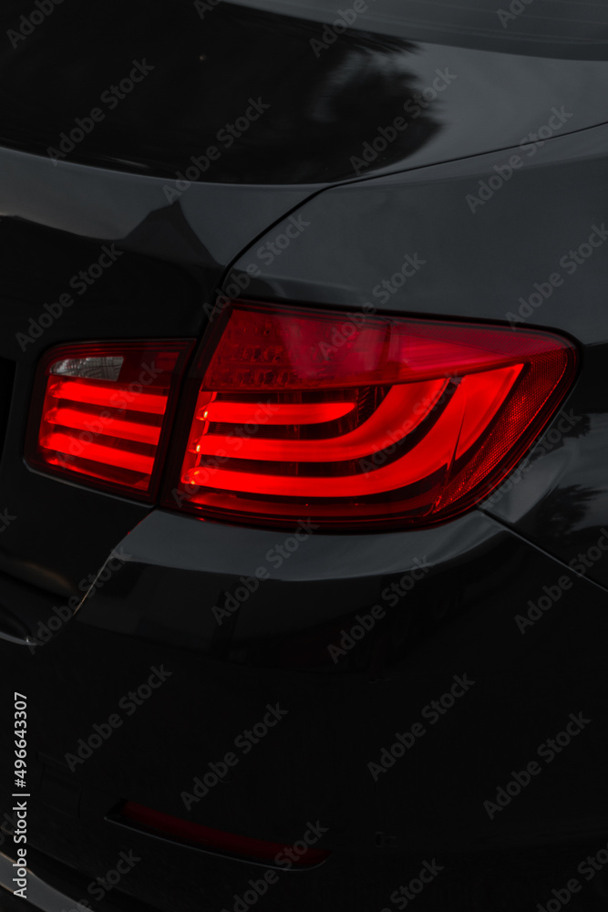 Stylish black metal car with a red brake light on a dark background. Beautiful transport wallpaper