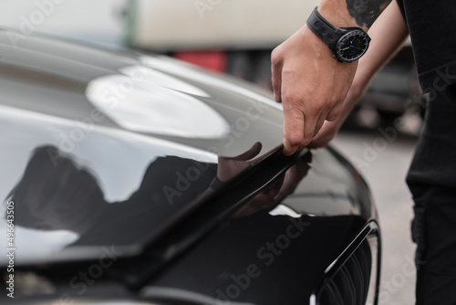 Man opens the hood of a black car, checking the engine and oils. Man's hands with a watch open the hood, close-up