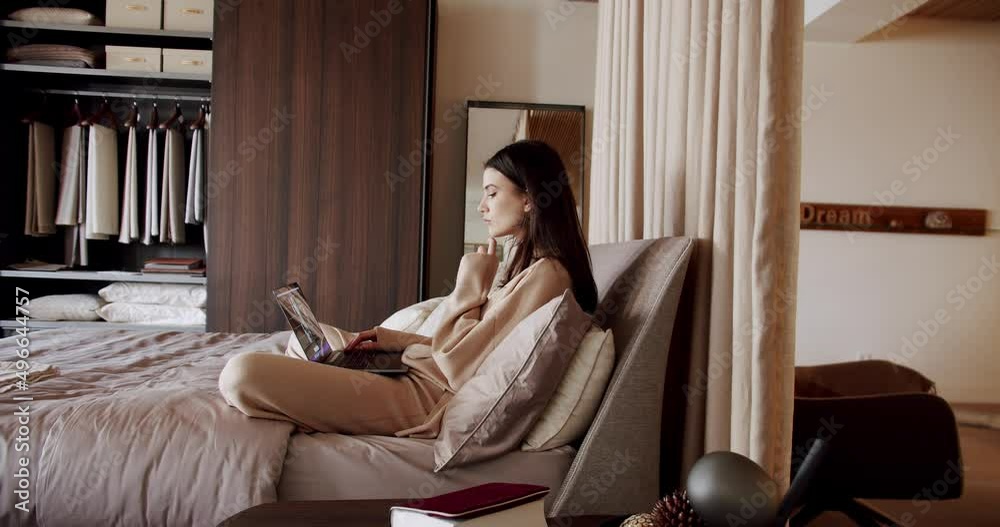 Young beautiful woman using laptop apps wear pyjama sitting in cozy bed in the morning browsing internet surfing web holding typing on computer device. Attractive woman typing on the keyboard, working Young beautiful woman using laptop apps wear pyjama sitting in cozy bed in the morning browsing internet surfing web holding typing on computer device. Attractive woman typing on the keyboard, working