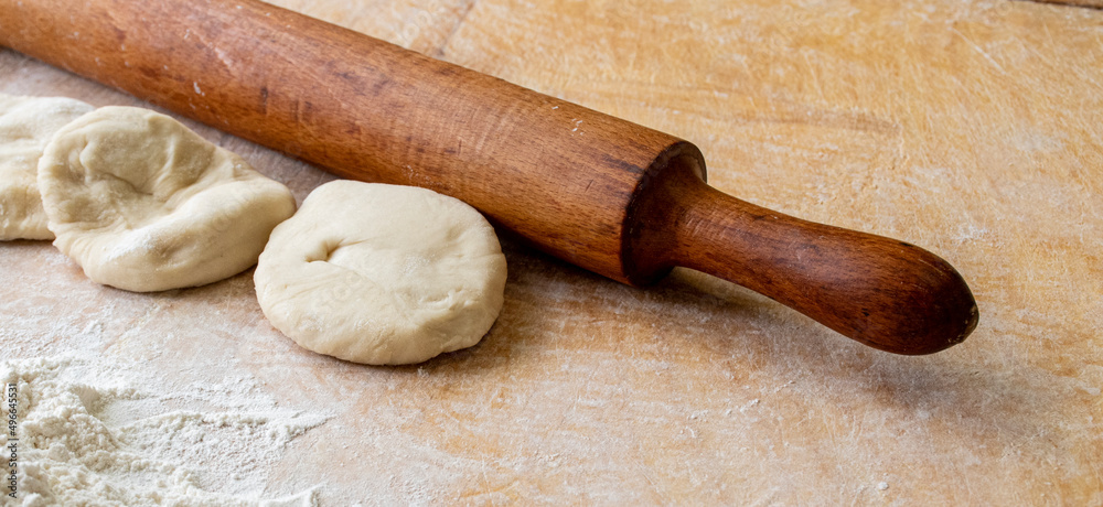 A rolling pin, raw dough and flour lie on a wooden table. The dough is being prepared for baking. A rolling pin, raw dough and flour lie on a wooden table. The dough is being prepared for baking.