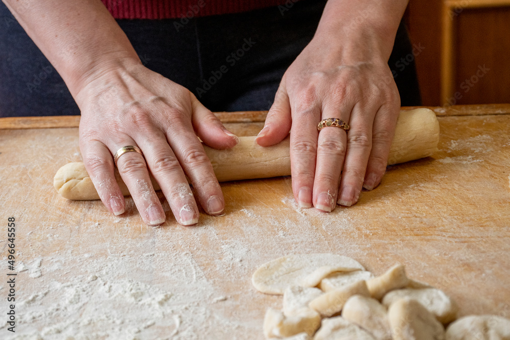 Female hands roll out raw pastry dough on a wooden board on the table.
