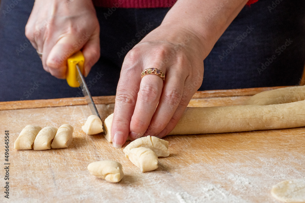 Cutting raw dough in flour with a knife. Close-up of woman hands cutting dough