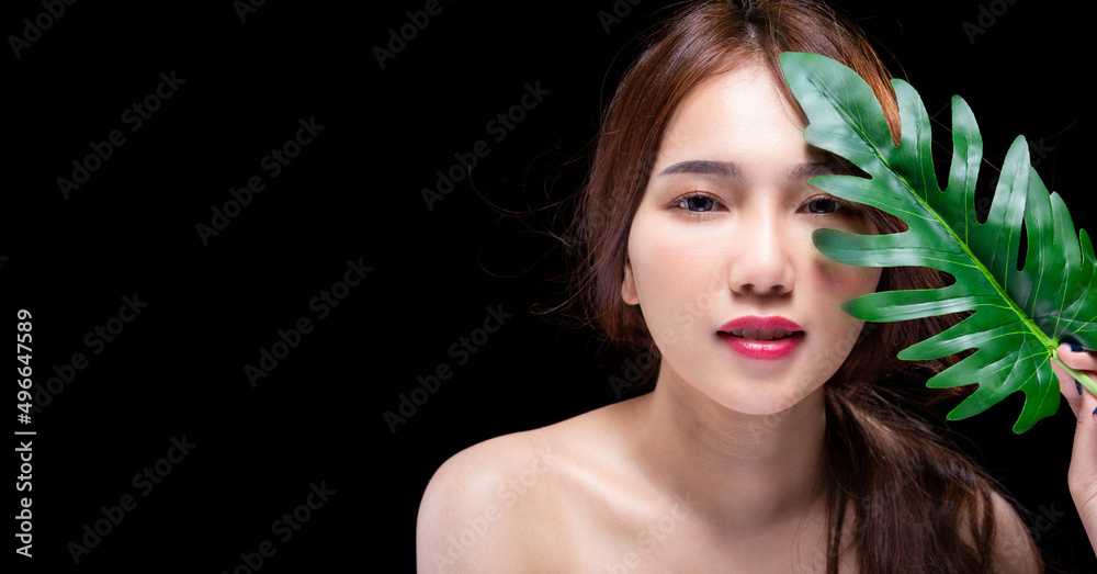 Beautiful young asian girl in studio on black background with beauty facial skin holds green tropical leaf in hands and covers a part of her beauty face Fashion beauty make up cosmetics Beautiful young asian girl in studio on black background with beauty facial skin holds green tropical leaf in hands and covers a part of her beauty face Fashion beauty make up cosmetics