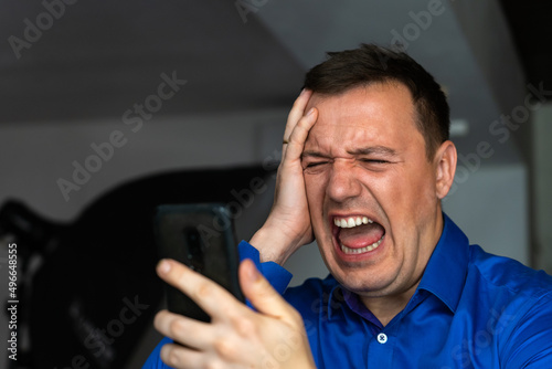 Caucasian man crying while looking at text message in cellphone. heartbroken millennial man looks at screen of smartphone and grieves. Tragedy in the family. Concept of Feeling Stressed, Anxiety