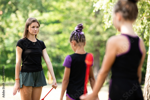 Coach demonstrating exercise with clubs to her trainees on rhythmic gymnastics training outdoors