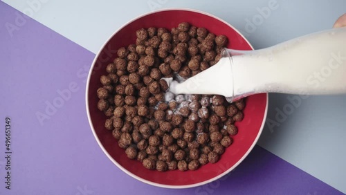 Milk pouring into sweetened rice cereal from glass into red bowl of with splashing in slow motion. Coco Pops, Rice Krispies that contains real chocolate. Cereal Breakfast for especially kids. photo