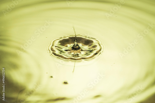 Beautiful macro view of drops making circles on water surface isolated on yellow background.