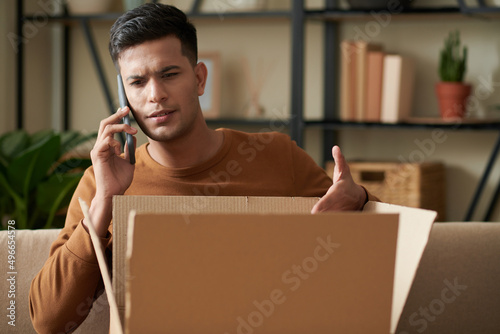 Angry young man calling to delivery service after receiving wrong package photo