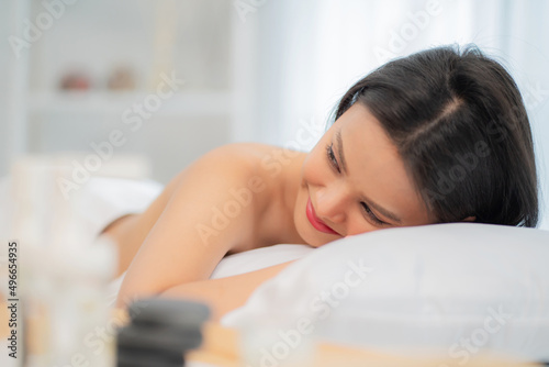 Beautiful woman getting spa oil massage lying on the massage bed in the therapy room at wellness center. Girl enjoy body treatment and looking at camera and smile. Relaxation and therapy concept.