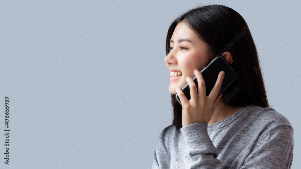 Happy Asian young woman talking on  phone with smile Beautiful girl looking to copy space during talking on mobile phone with gray background Use for advertisement
Female get a conversation to someone
