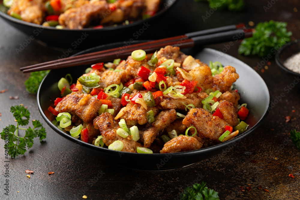 Stir fry salt and pepper pork loin with herbs in black bowl. Asian food