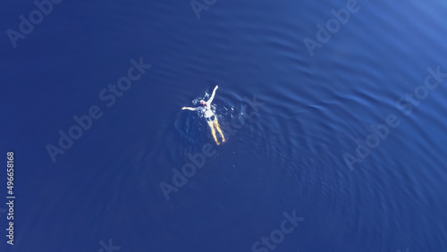 Woman swimming in a clear blue lake on a hot summers day. Birds eye view.