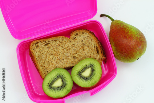Lunchbox containing brown bread sandwich, two kiwi halves and pear on white background
